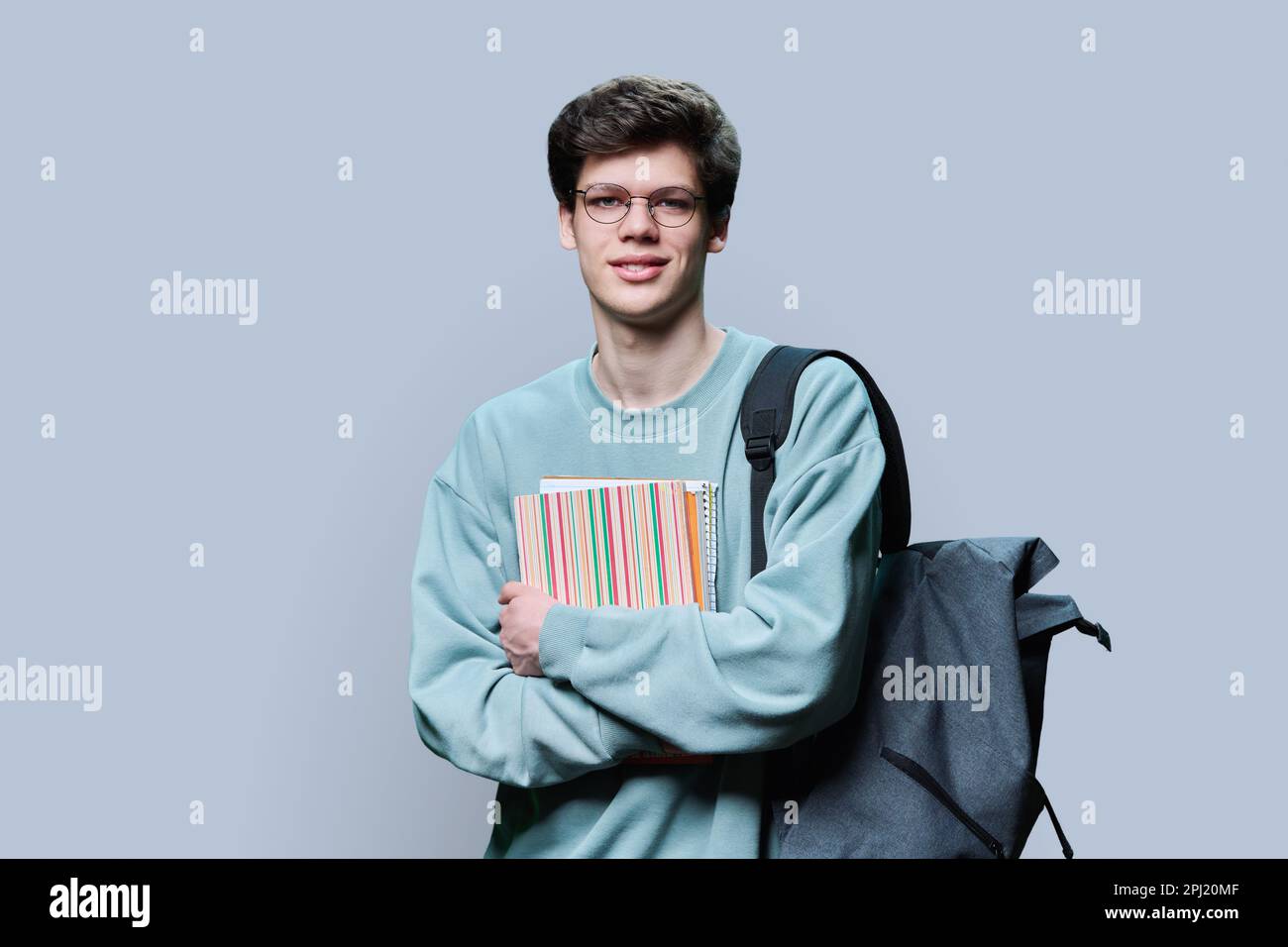 Porträt eines jungen männlichen College-Studenten mit Brille und Rucksack auf grauem Hintergrund Stockfoto