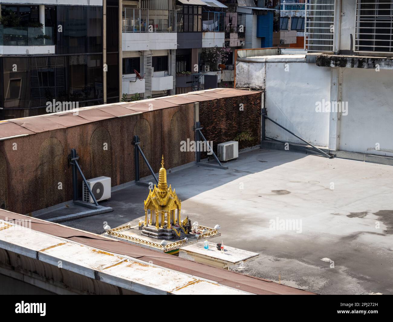 Hoch über den belebten Straßen von Bangkok steht ein kleiner goldener buddhistischer Tempel auf einem Dach, eine ruhige Familienoase inmitten des Chaos von Bangkok Stockfoto