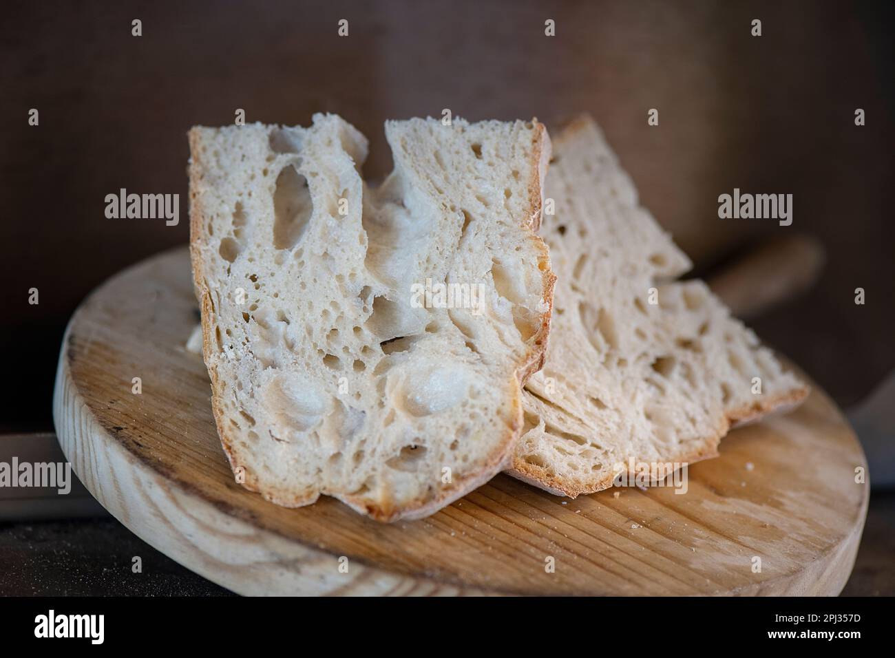 Rustikale hausgemachte Sauerteigbrotscheiben auf einem runden Holzbrett, gesunder und leckerer Laib mit einer wunderschönen goldenen Kruste und einem leichten und luftigen Krümel Stockfoto