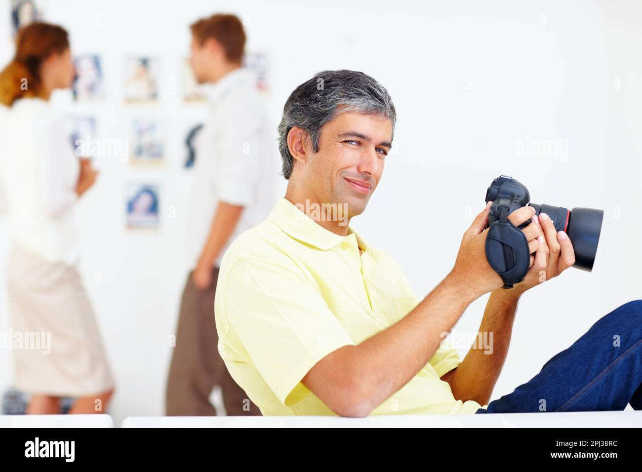 Fotograf, der Fotos in der Kamera ansieht. Porträt eines lächelnden Fotografen, der Fotos in seiner Kamera mit Kollegen im Hintergrund ansieht. Stockfoto