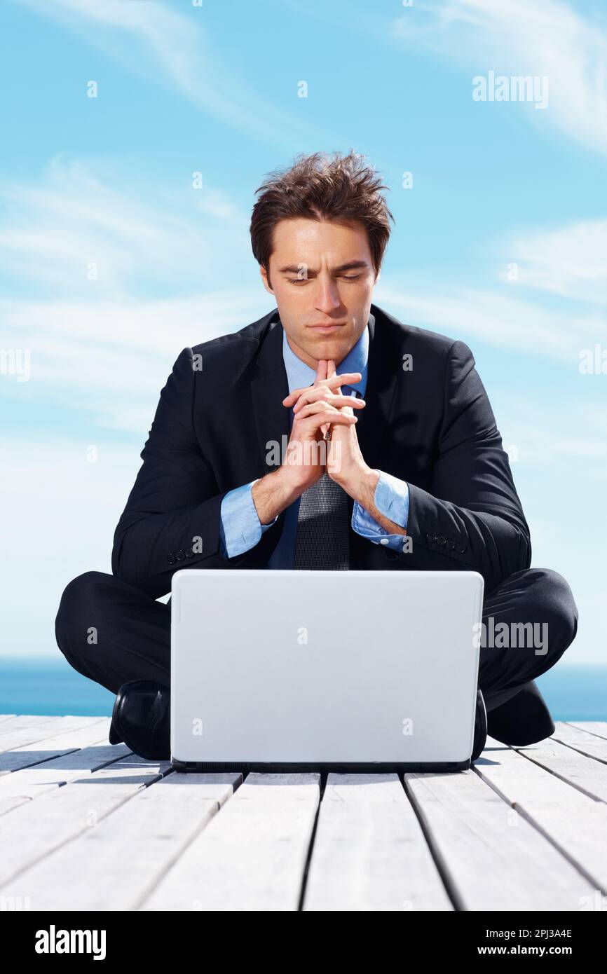 Ein seriöser junger Geschäftsmann, der im Freien ein Notebook benutzt. Ein seriöser junger Geschäftsmann, der im Freien ein Notebook benutzt. Stockfoto