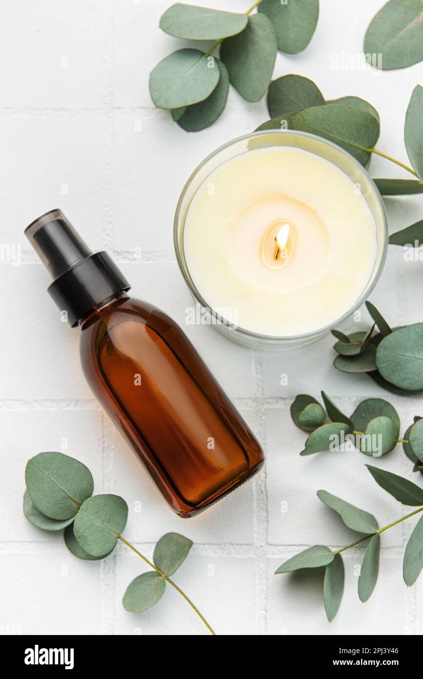 Flasche mit natürlichem Kosmetiköl, Aromakerze und Eukalyptusblättern auf weißem Fliesenhintergrund. Stockfoto