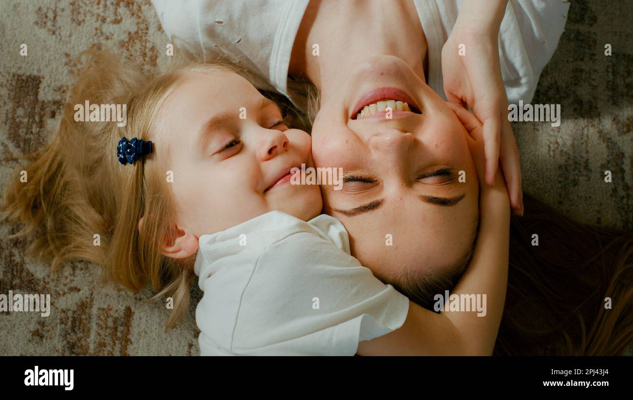 Süßes, liebevolles, adoptiertes Kind, Vorschulmädchen, das kuschelige Mutter umarmt, mit Kopfansicht. Kind Tochter mit Mutter zwei Gesichter kuscheln zu Hause Stockfoto