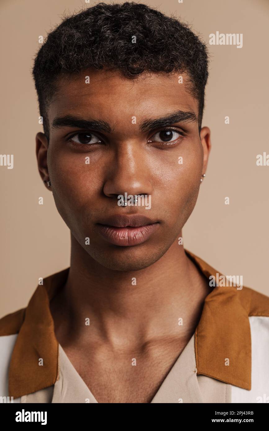 Porträt eines jungen, gutaussehenden, seriösen afrikaners mit einem Piercing, der in die Kamera schaut, während er über einem isolierten beigen Hintergrund steht Stockfoto