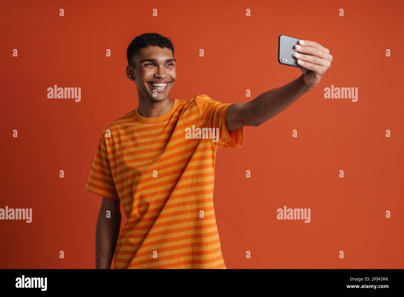 Junger, gutaussehender, glücklicher afrikaner mit Piercing, der Selfie am Telefon macht, während er über einem isolierten orangefarbenen Hintergrund steht Stockfoto