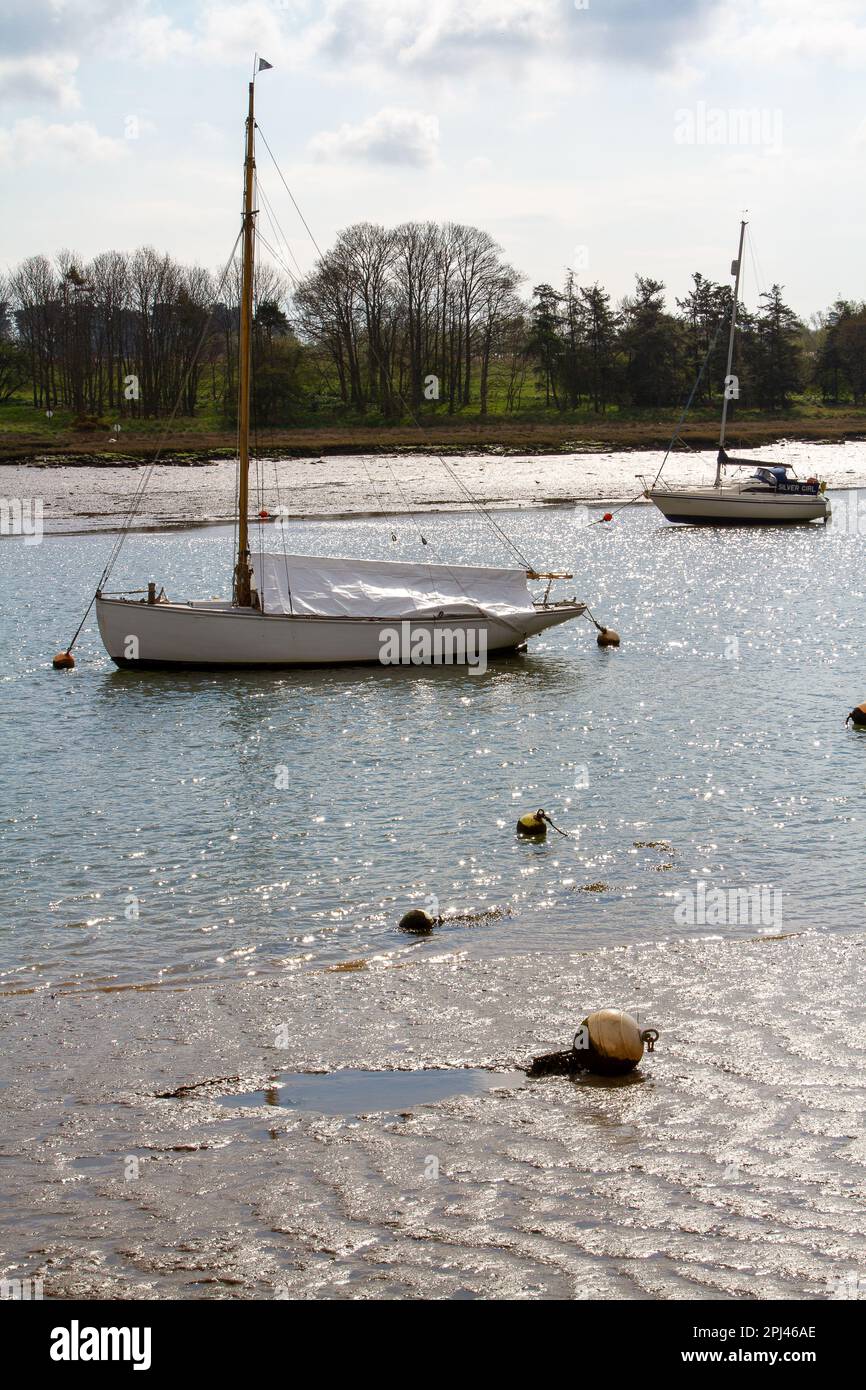 Zwei kleine Segelboote verlegten bei Ebbe am Fluss Deben, während das Sonnenlicht vom Wasser glitzert Stockfoto