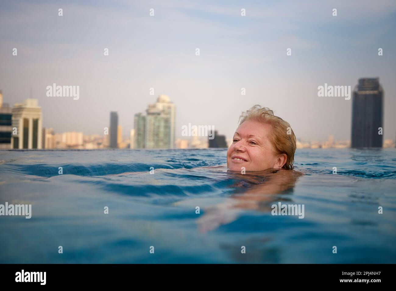 Aktive Seniorin schwimmt im Pool mit Blick auf die moderne Stadt. Stockfoto