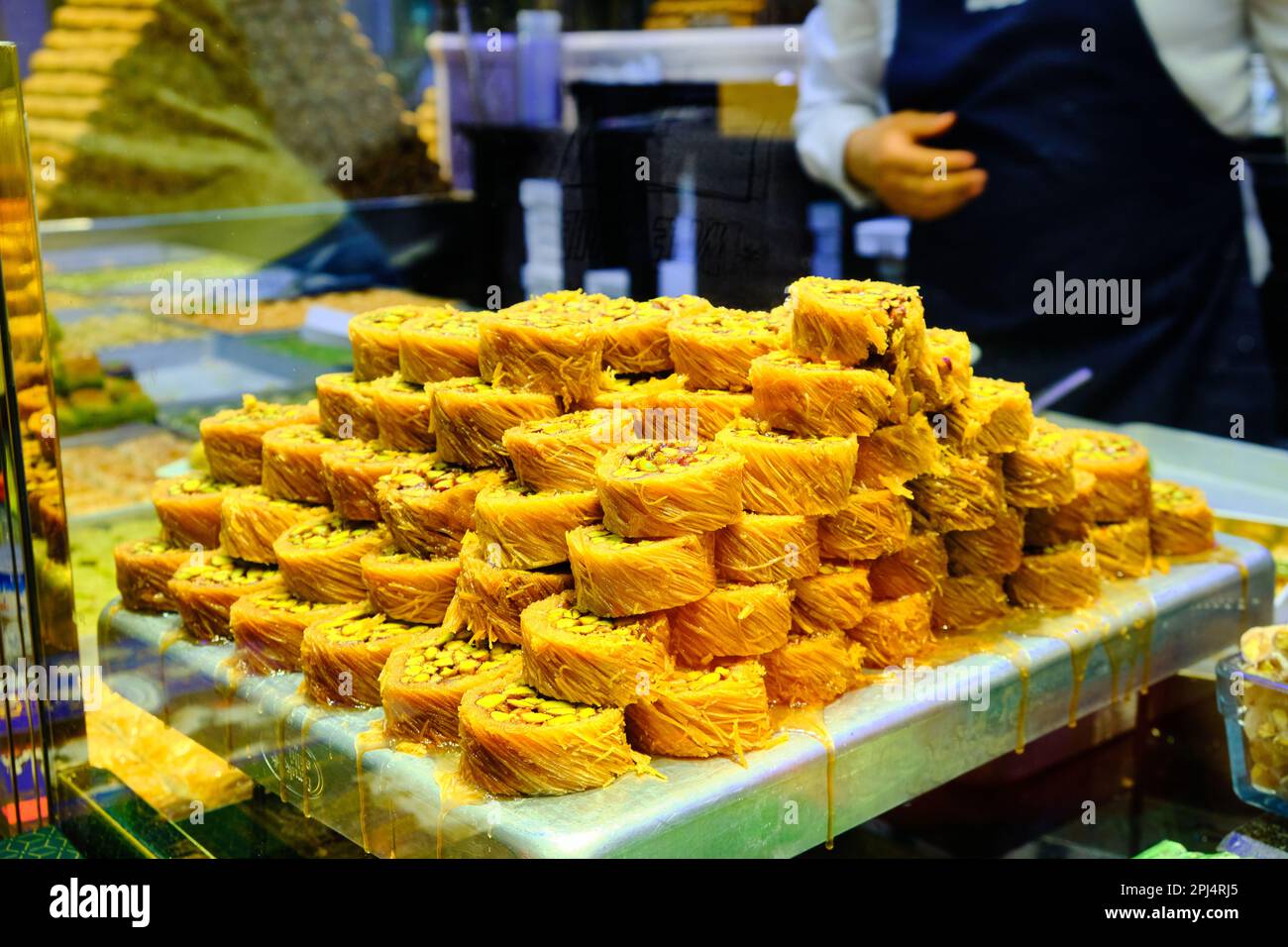 Stapel Baklava im Vordergrund und die Hände eines unbekannten Verkäufers bedienen die Gäste im traditionellen türkischen Delights Shop. Eine Schachtel türkischer Konfetti Stockfoto