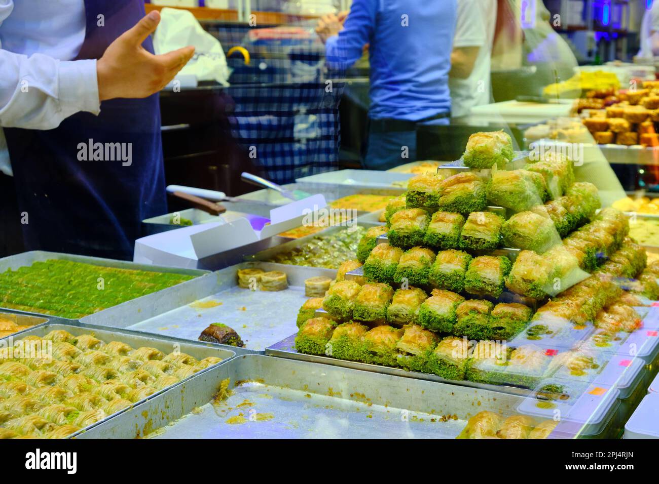 Stapel Baklava im Vordergrund und die Hände eines unbekannten Verkäufers bedienen die Gäste im traditionellen türkischen Delights Shop. Eine Schachtel türkischer Konfetti Stockfoto