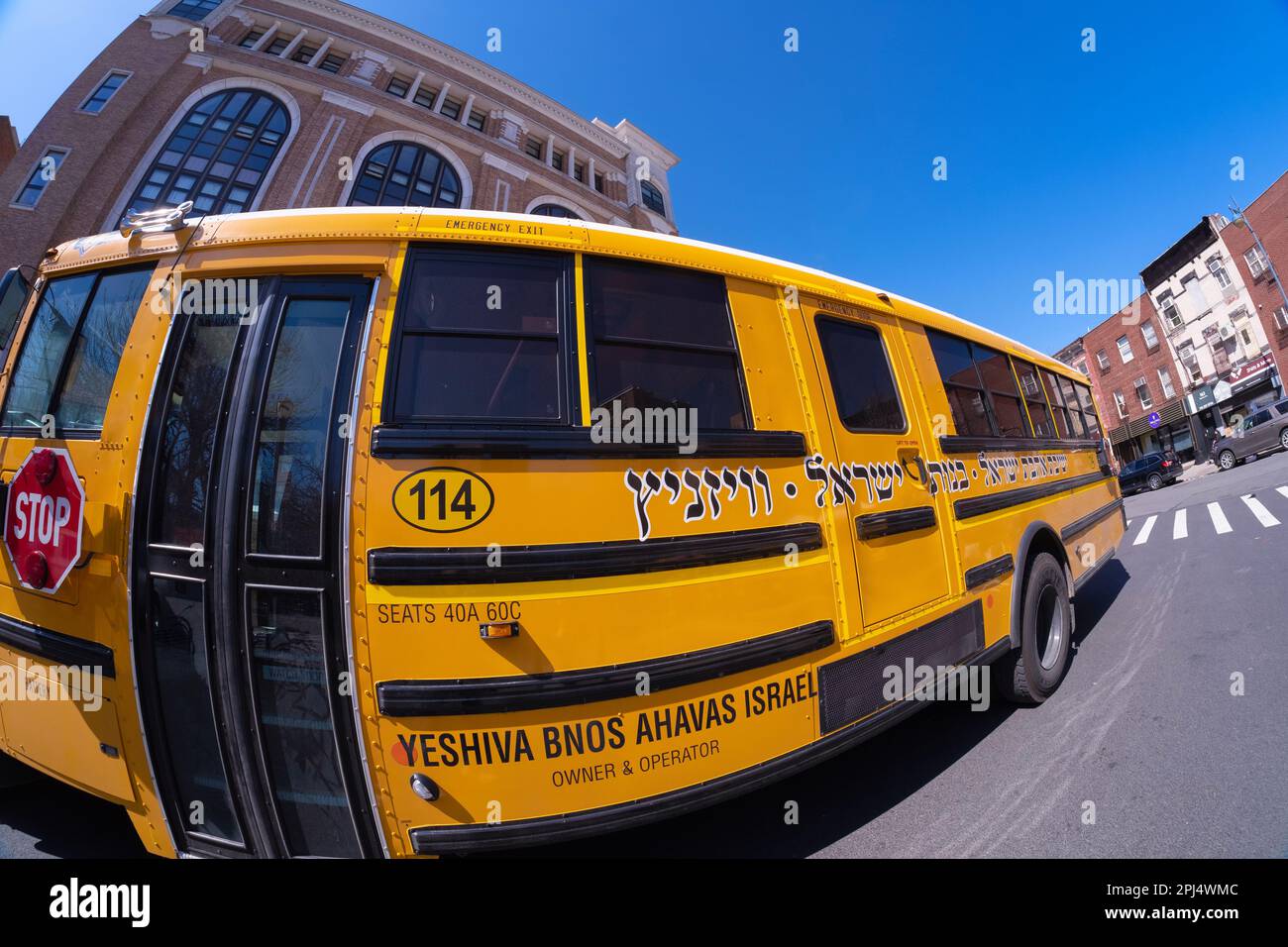 Fischaugenlinsen-Blick auf einen Vizhnitz-Schulbus mit jiddischer Schrift und deren Schule im Hintergrund. Vizhnitz ist das Wort ganz links. In Brooklyn, New York. Stockfoto