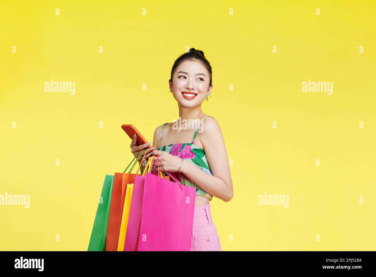 Eine schöne Asiatin hält Einkaufstaschen und ein Handy mit Gesicht in der Hand Stockfoto