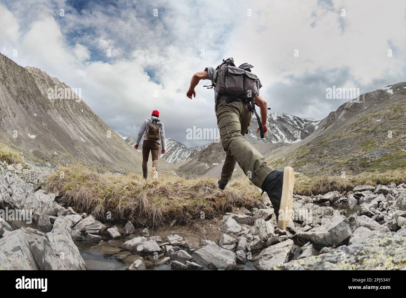 Zwei junge Wanderer wandern mit leichten Rucksäcken in den Bergen. Touristen springen über das Hindernis Stockfoto