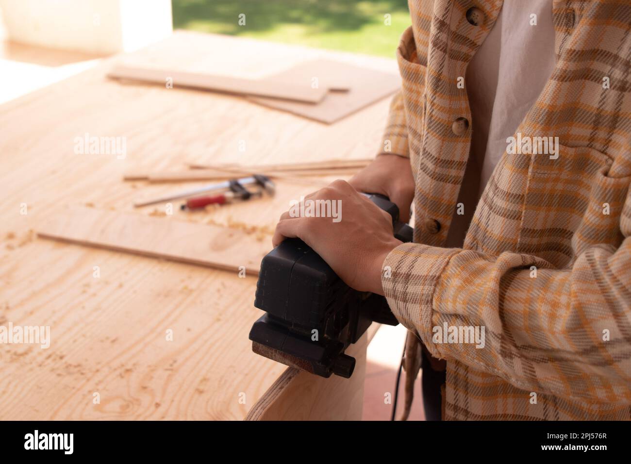 Seitenansicht des Ernteguts nicht erkennbarer männlicher Holzarbeiter, der Holzbretter mit einer elektrischen Stichsäge auf der Werkbank schneidet, während er Möbel im Arbeitsraum befestigt Stockfoto
