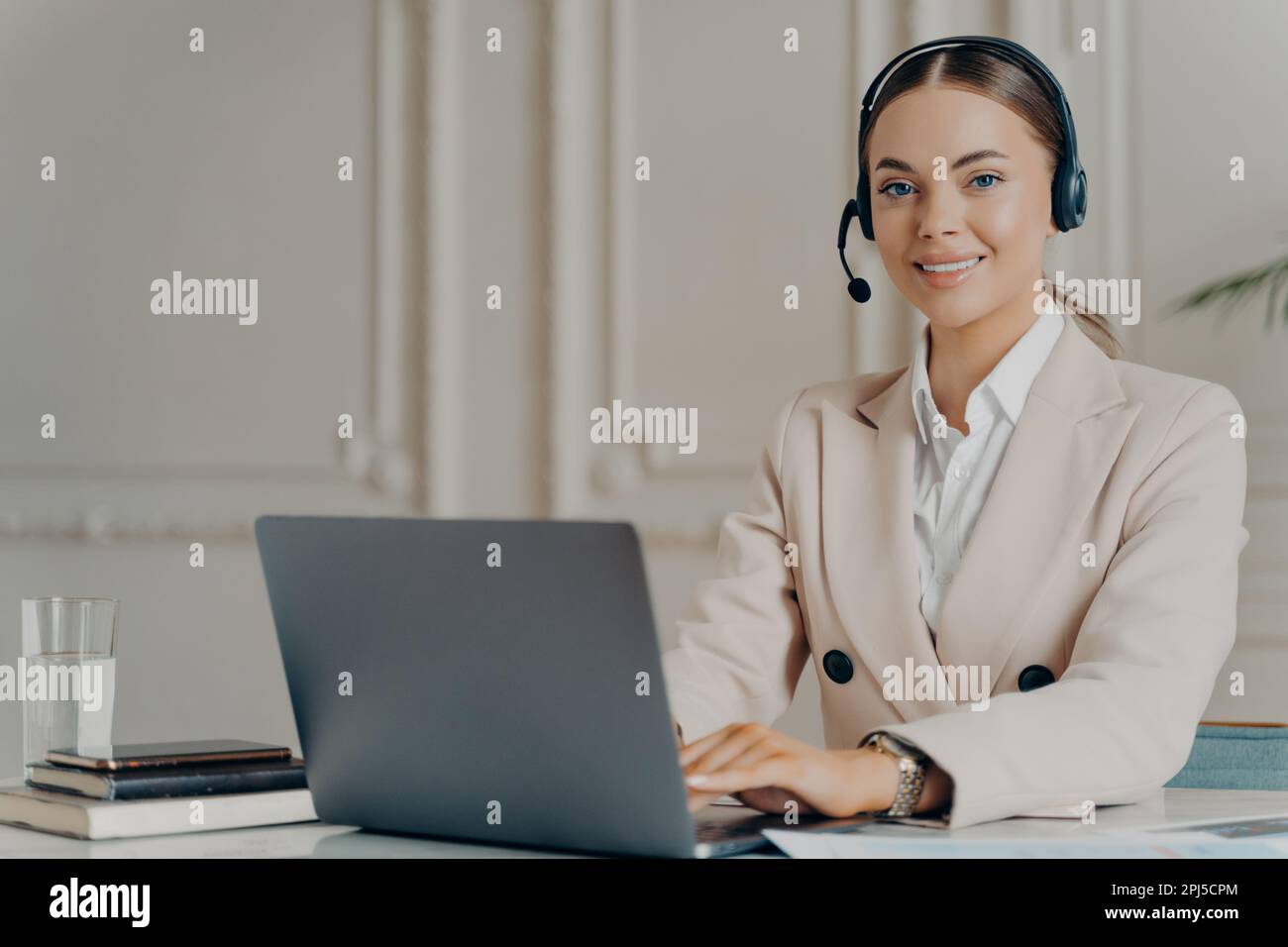 Fröhliche Kundenbetreuerin, die in einem modernen Callcenter am Computer arbeitet, glückliche Geschäftsfrau, die vor der Kamera lächelt, während sie auf ihm sitzt Stockfoto