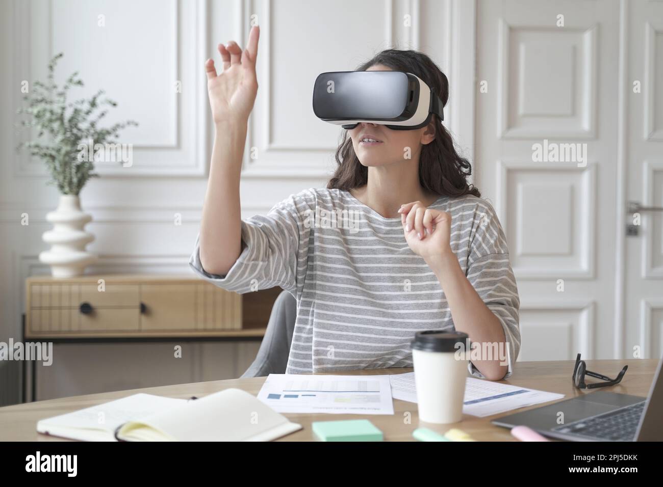 VR-App für die Arbeit. Junge fokussierte Frau mit Virtual-Reality-Headset, die 360-Grad-Inhalte ansieht und während des Sitzes in eine simulierte Umgebung eintaucht Stockfoto