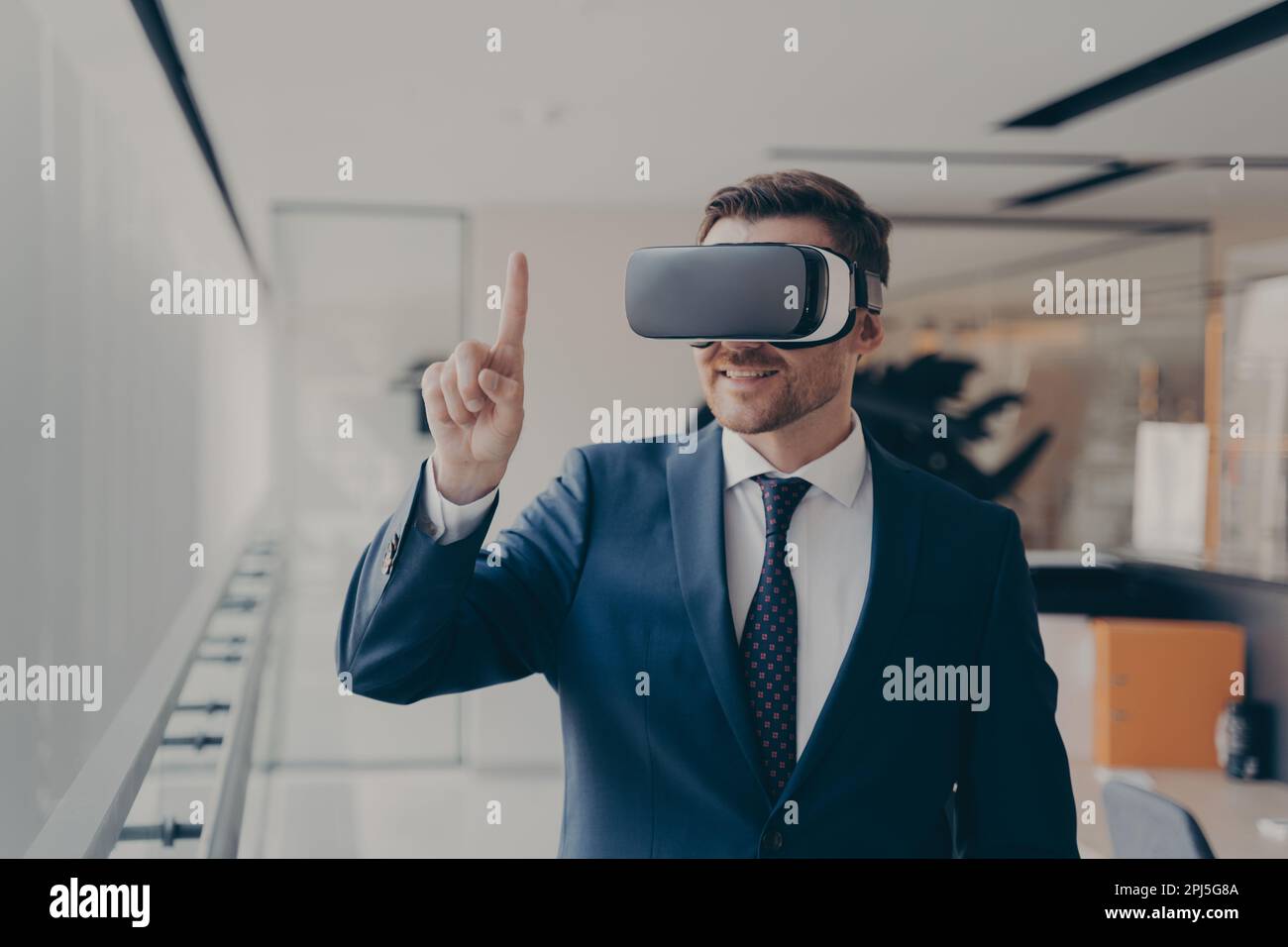 Lächelnder, bärtiger Büroangestellter im Anzug trägt VR-Brille arbeitet in Augmented Reality im Büro, Geschäftsmann in 3D-Brille interagiert mit Cyber Stockfoto