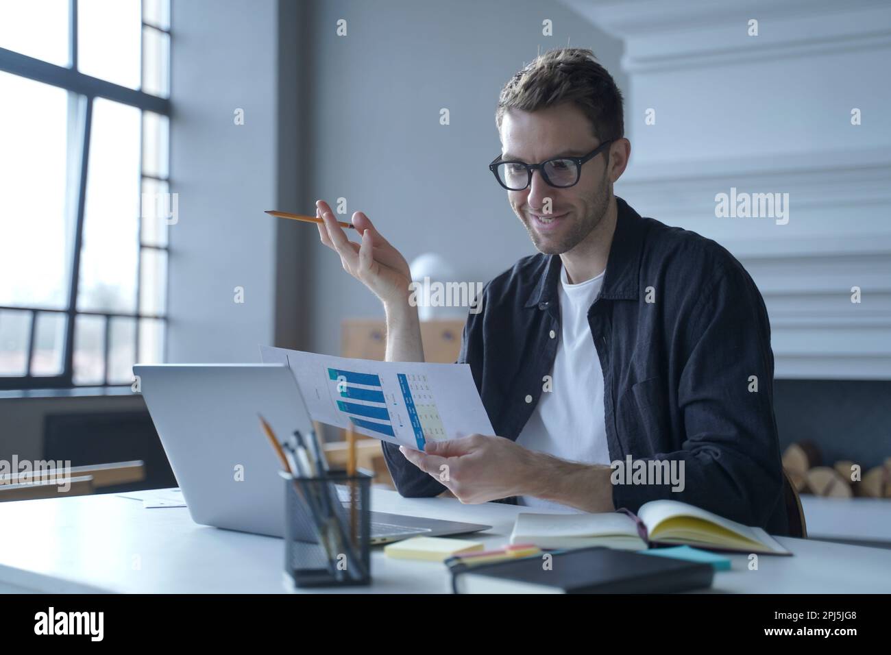 Ein junger, zufriedener österreichischer Geschäftsmann mit Brille, der den letzten Geschäftsbericht mit der Vertriebsabteilung über Videogespräche auf einem Laptop-Computer bespricht Stockfoto