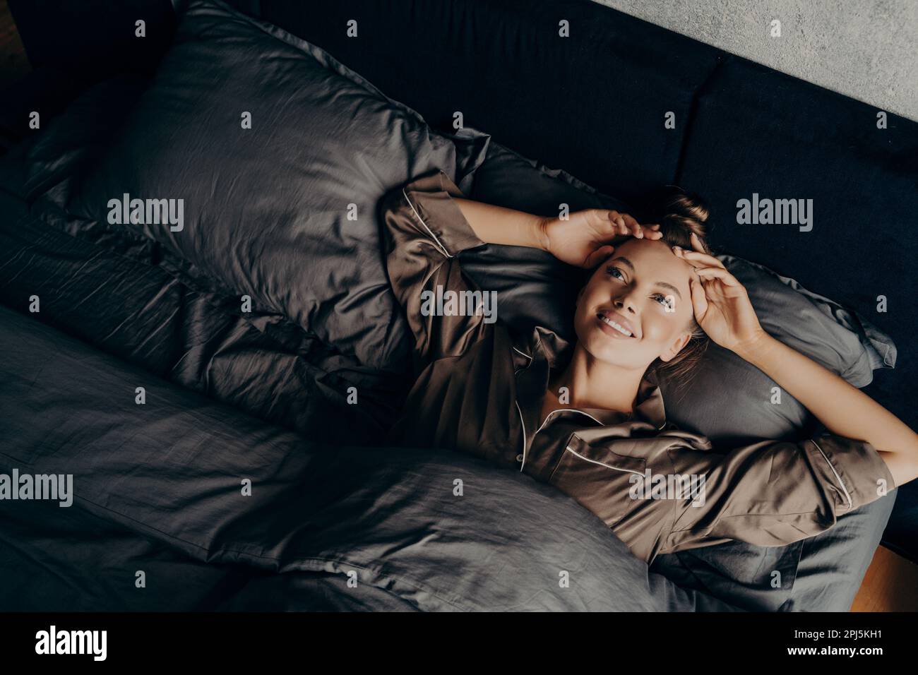 Bild eines jungen, wunderschönen, verschlafenen Mädchens in einem satinbequemen Pyjama, das am frühen Morgen im bequemen Bett aufwacht und sich am neuen Tag freut, glücklich und breit Stockfoto