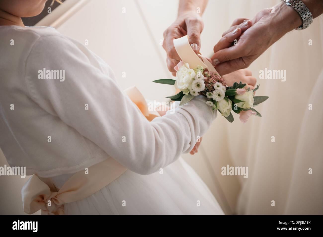 Eine lächelnde Brautjungfer hilft einem jungen Mädchen, indem sie eine Blumenapplikation sicher an ihrem Handgelenk befestigt Stockfoto