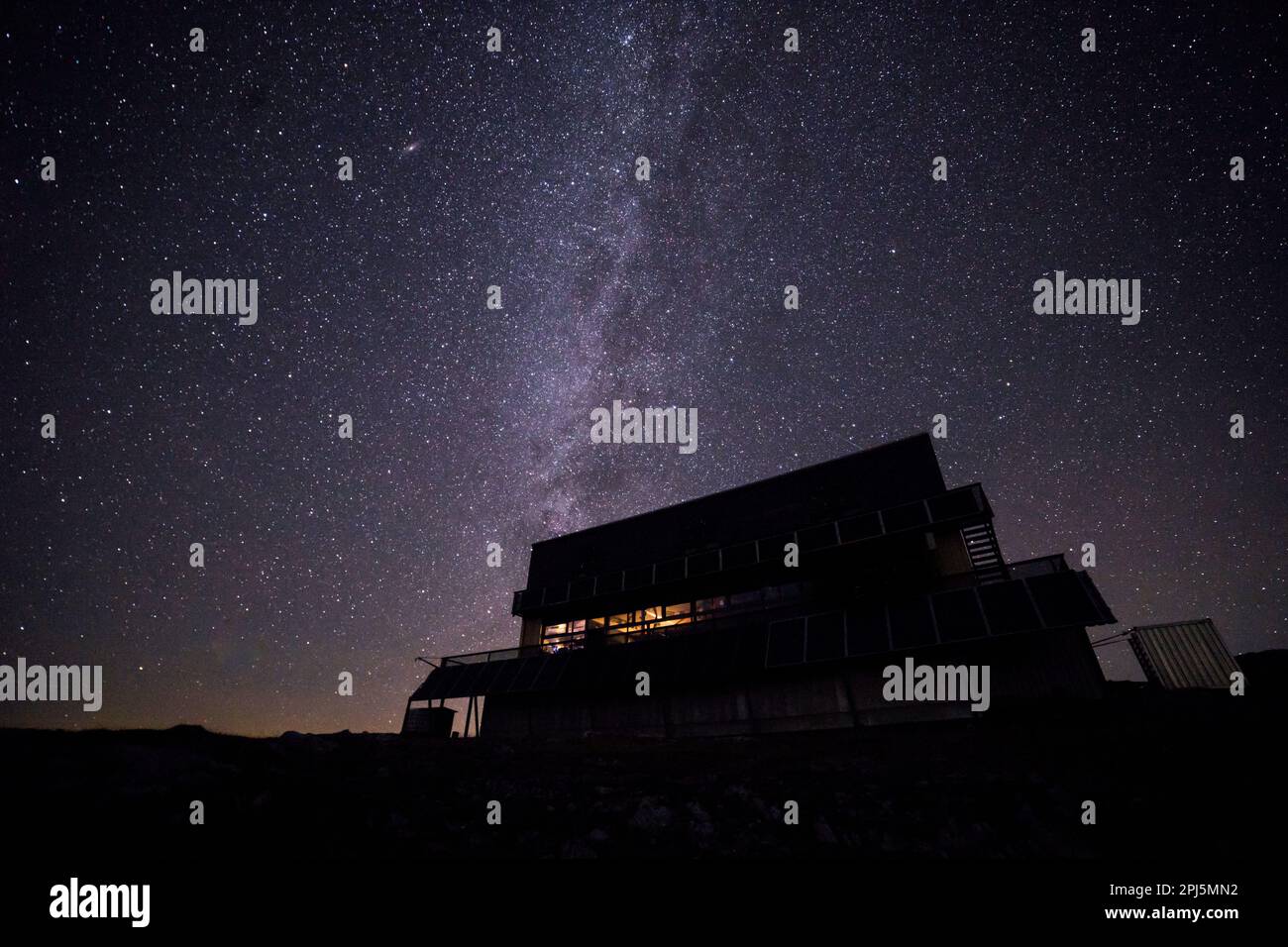 Der ruhige Nachthimmel wird von einer hellen, milchigen Kulisse beleuchtet, mit einem gemütlichen Haus im Vordergrund Stockfoto