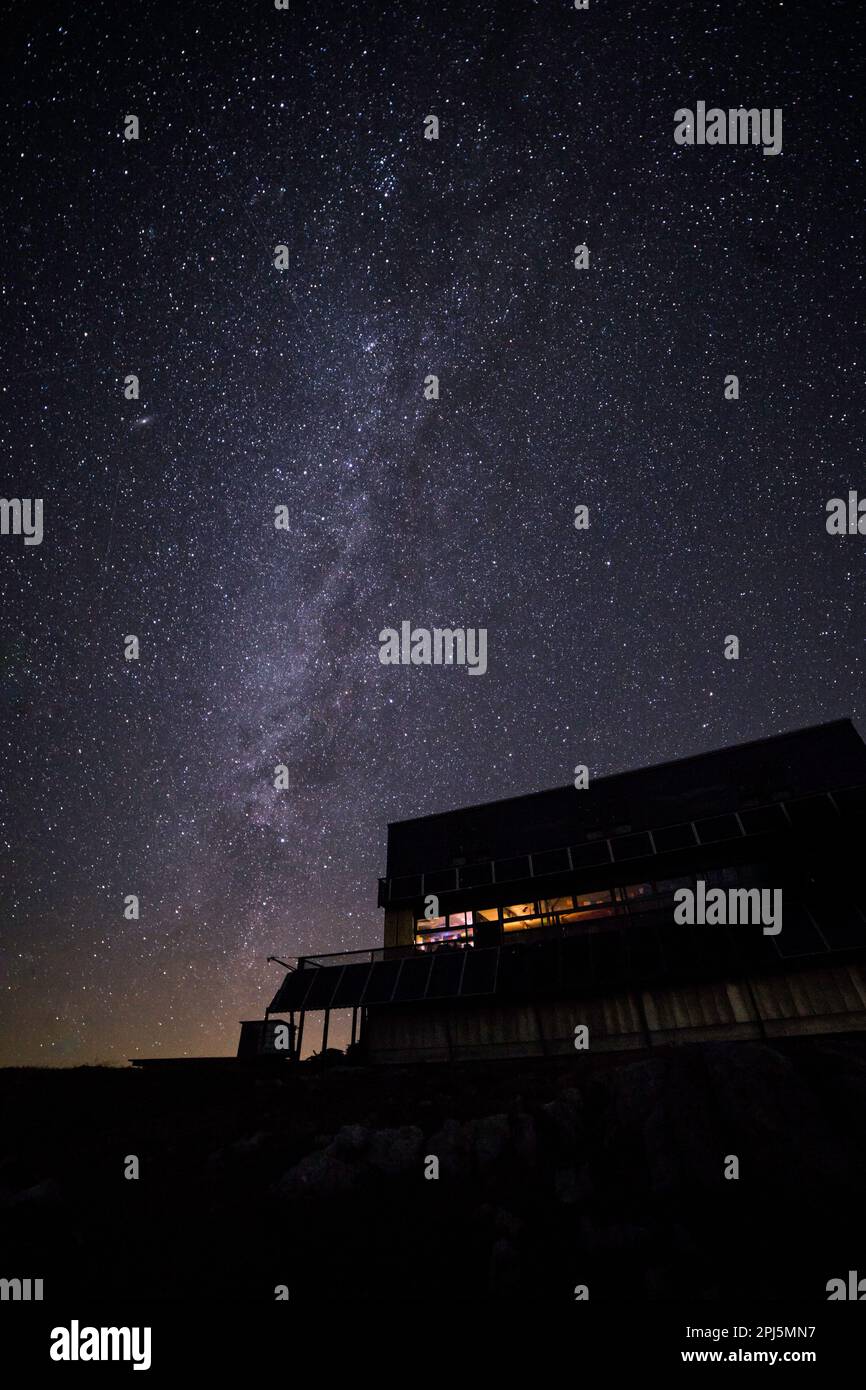 Der ruhige Nachthimmel wird von einer hellen, milchigen Kulisse beleuchtet, mit einem gemütlichen Haus im Vordergrund Stockfoto