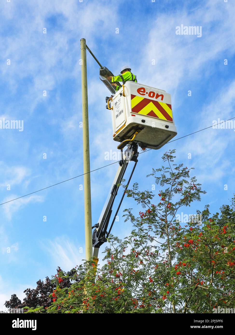 Ein EON-Mitarbeiter, der eine Straßenbeleuchtung hoch oben auf einem Kirschpflücker repariert, einem Hydraulikkran mit Geländerplattform am Ende, England, Großbritannien Stockfoto