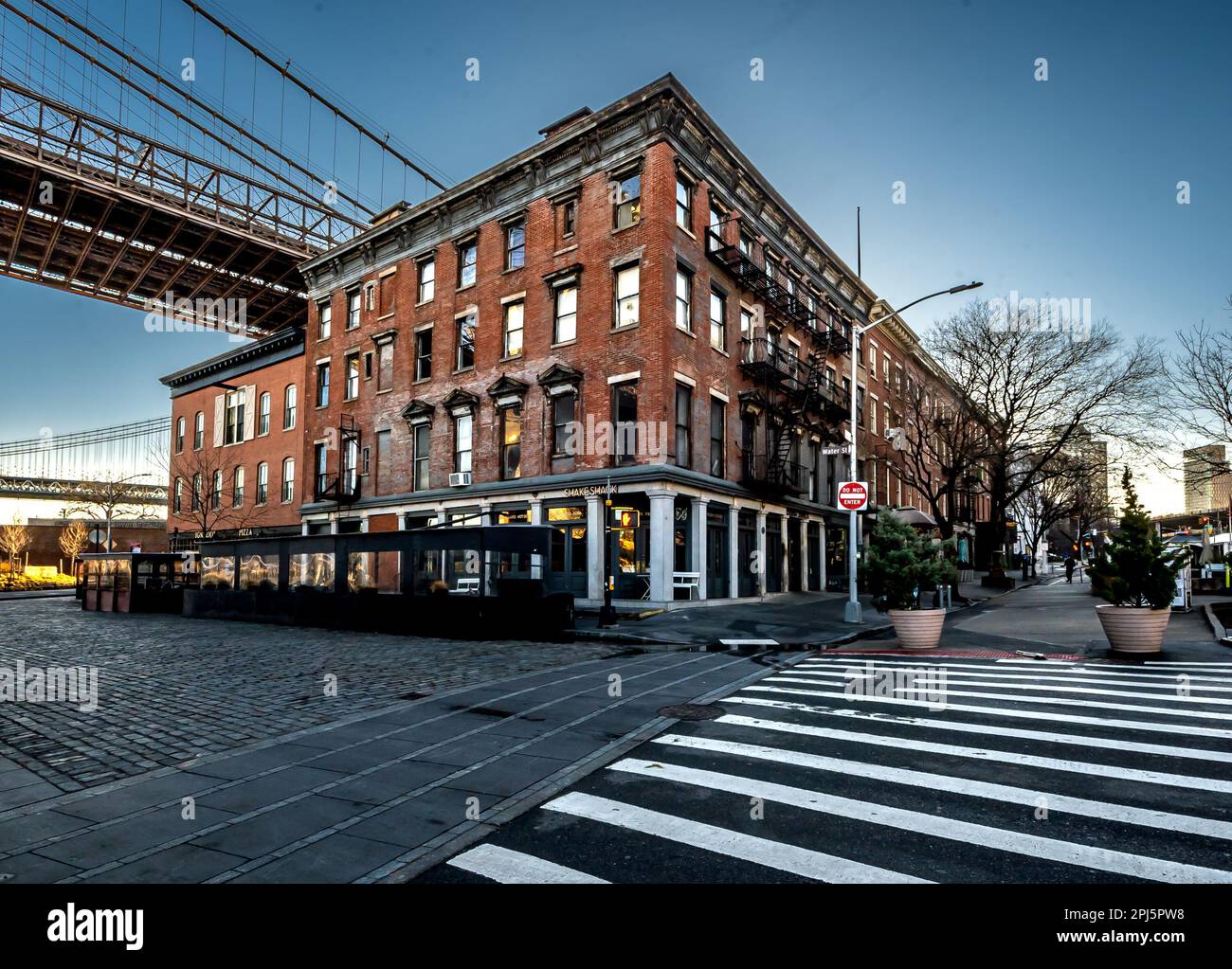 Brooklyn, NY - USA - 26. März 2023 Sonnenaufgang mit roten Backsteingebäuden an der Ecke Old Fulton Street und Water Street unter der Brooklyn Bridge Stockfoto