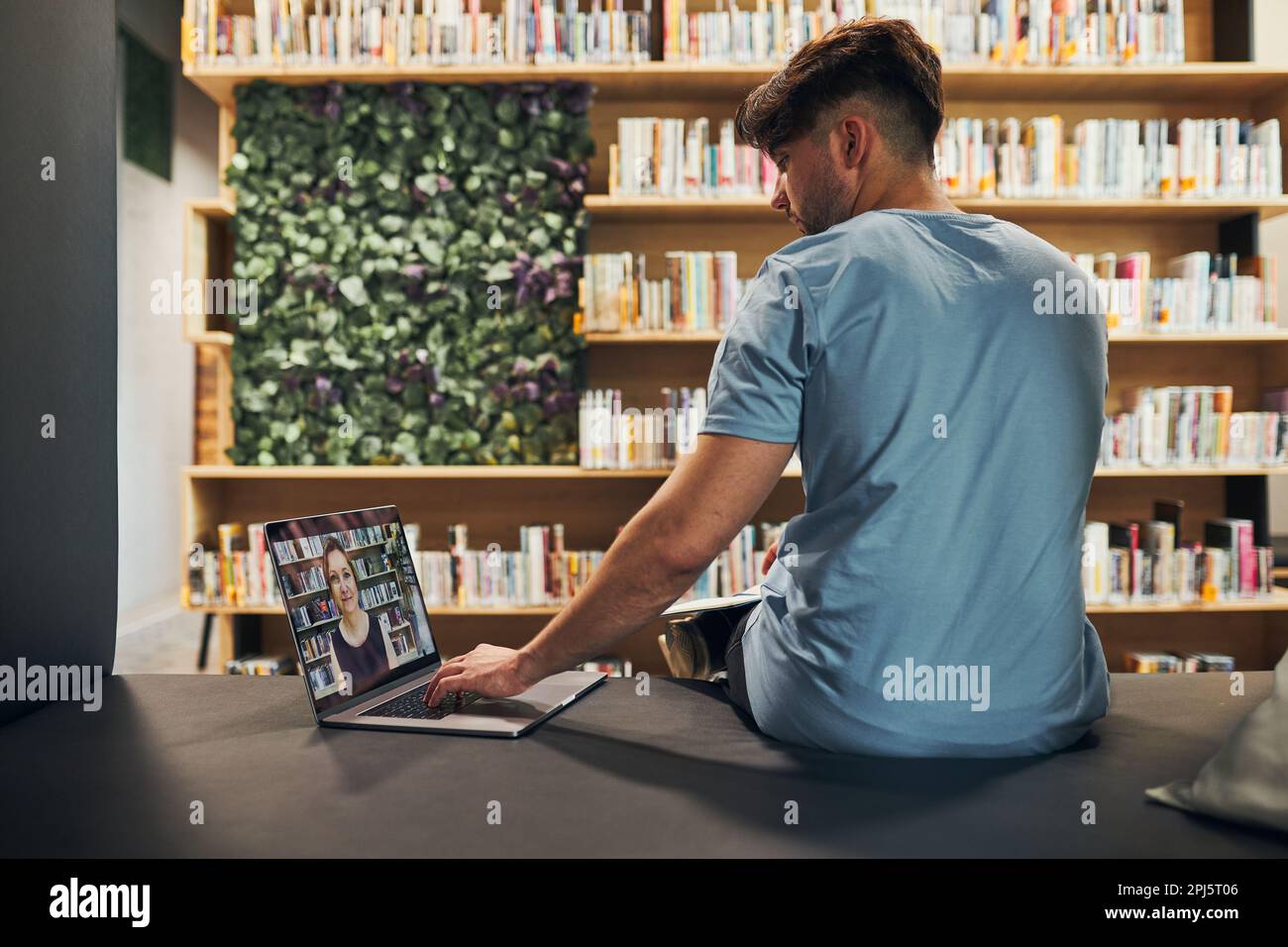Student lernt in der Universitätsbibliothek. Junger Mann, der Videokurs auf einem Laptop hat. Mann hört sich Online-Kurs an. Fokussierter Student, der für das College lernt Stockfoto