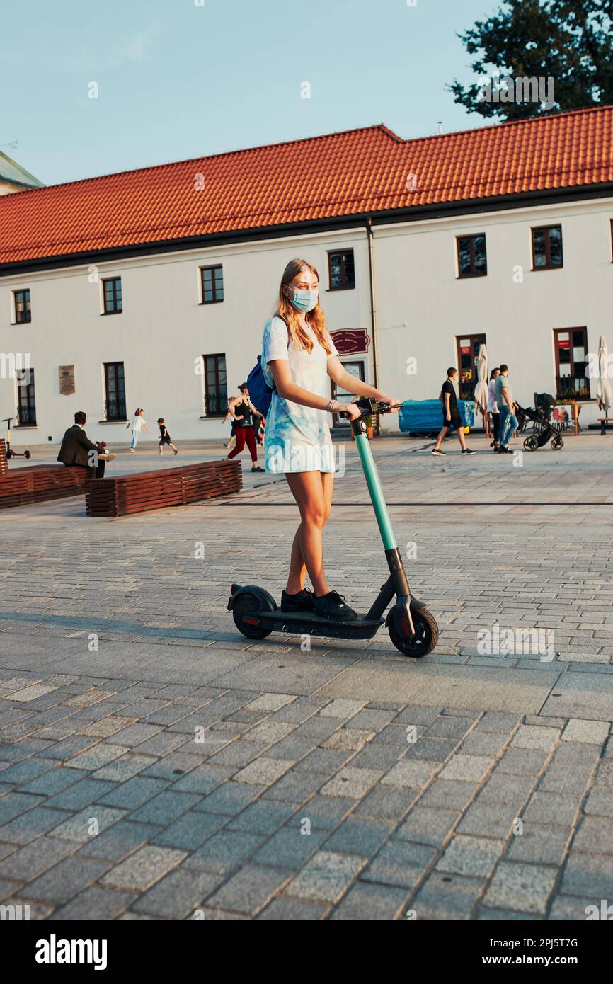 Junge Frau auf einem Elektroroller im Stadtzentrum. Frau trägt die Gesichtsmaske, um eine Virusinfektion zu vermeiden und die Ausbreitung der Krankheit zu verhindern i Stockfoto