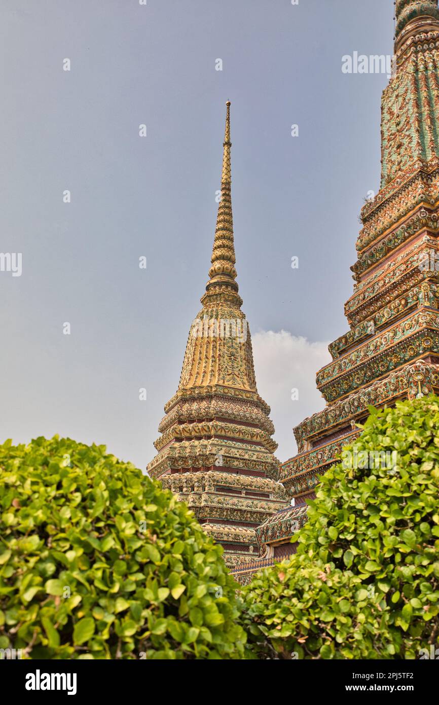 Wunderschöne, detaillierte Türme mit vielen Ornamenten am Wat Pho Tempel in Bangok in Thailand, in den Vordergrundbüschen. Stockfoto