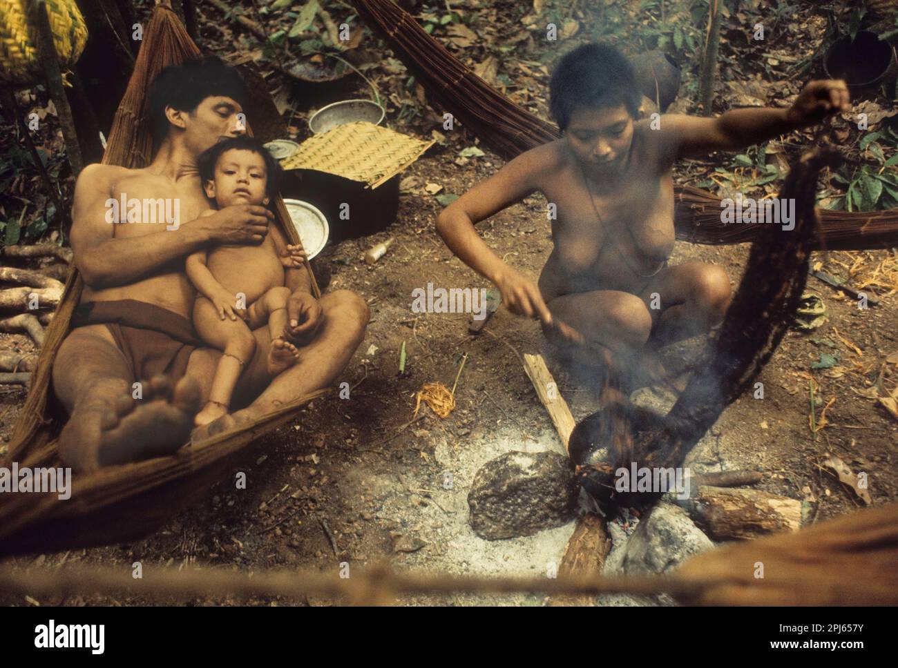 Indigene Völker Venezuelas: Stamm der Eñepa (Panare): Familie im Lager im Regenwald: Mann in Hängematte mit Kind, Frau, die eine Wachsfackel herstellt. Stockfoto