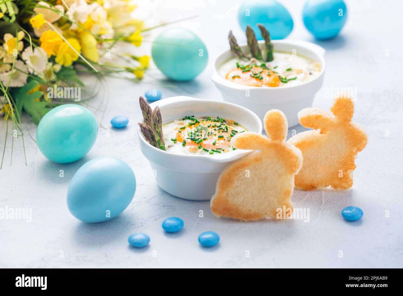 Geraffte Eier (Oeuf-Kokotte) Oder gebackene Eier mit grünem Spargel mit Ostergebäck Und Eier Stockfoto