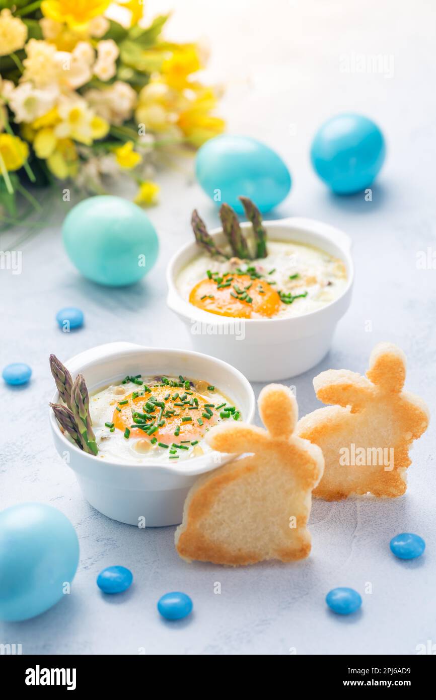 Geraffte Eier (Oeuf-Kokotte) Oder gebackene Eier mit grünem Spargel mit Ostergebäck Und Eier Stockfoto