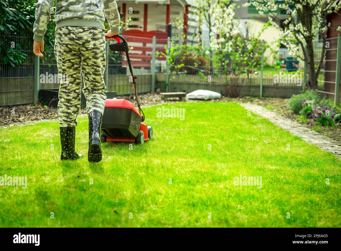 Rasenpflege - Teenager Rasenschnitt im kleinen Garten mit Elektrischer Rasenmäher Stockfoto