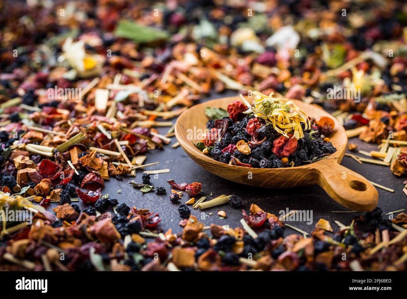 Getrocknete Teeblätter, Früchte und Beeren in Schale auf rustikalem Holztisch Stockfoto