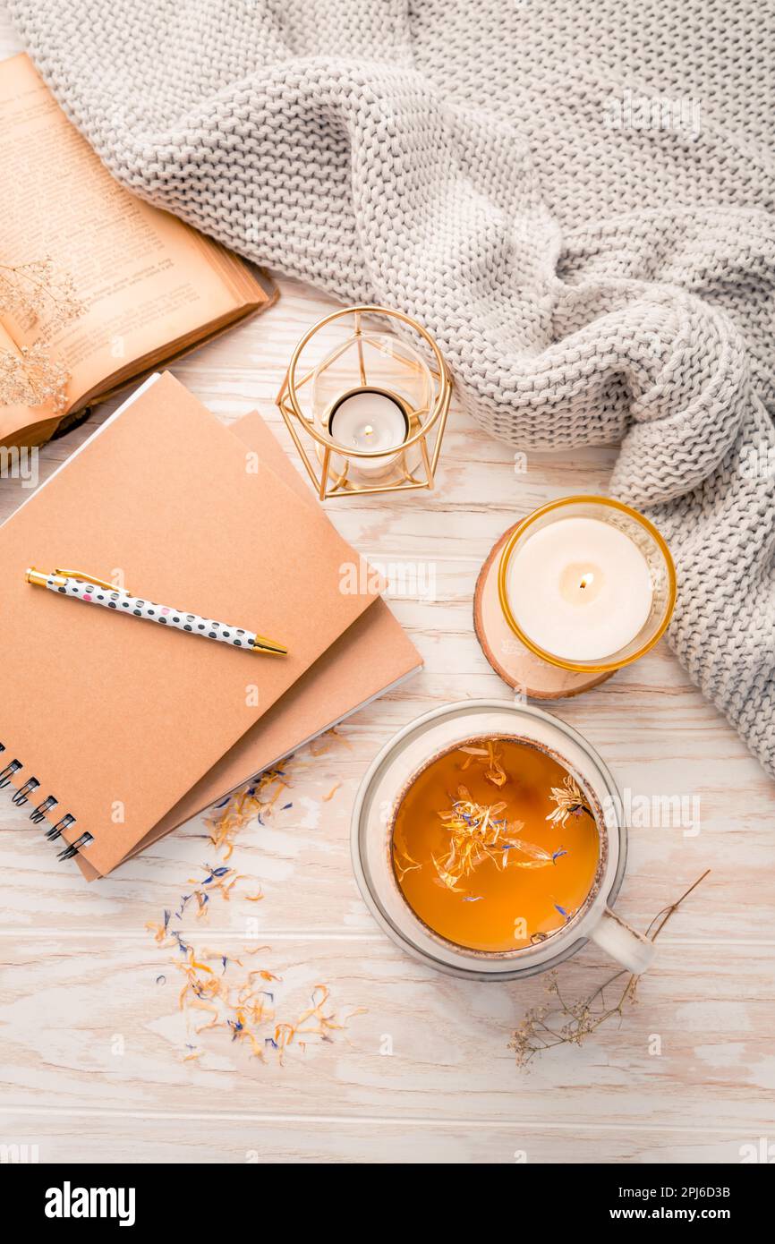 Heißer Kräutertee mit Notizblock, Kerze, Buch und Decke. Gemütlicher und hygge Lebensstil Stockfoto