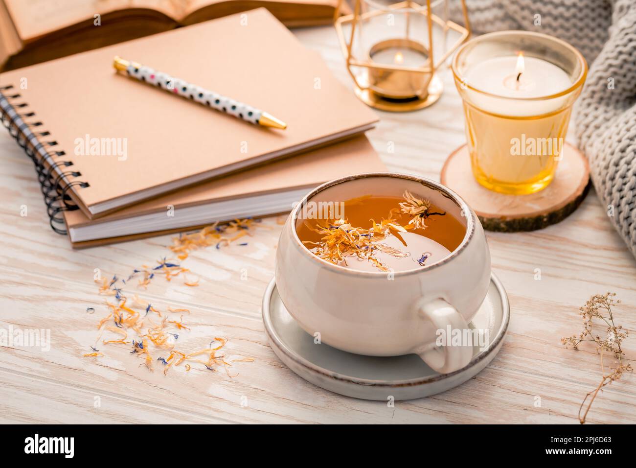 Heißer Kräutertee mit Notizblock, Kerze, Buch und Decke. Gemütlicher und hygge Lebensstil Stockfoto