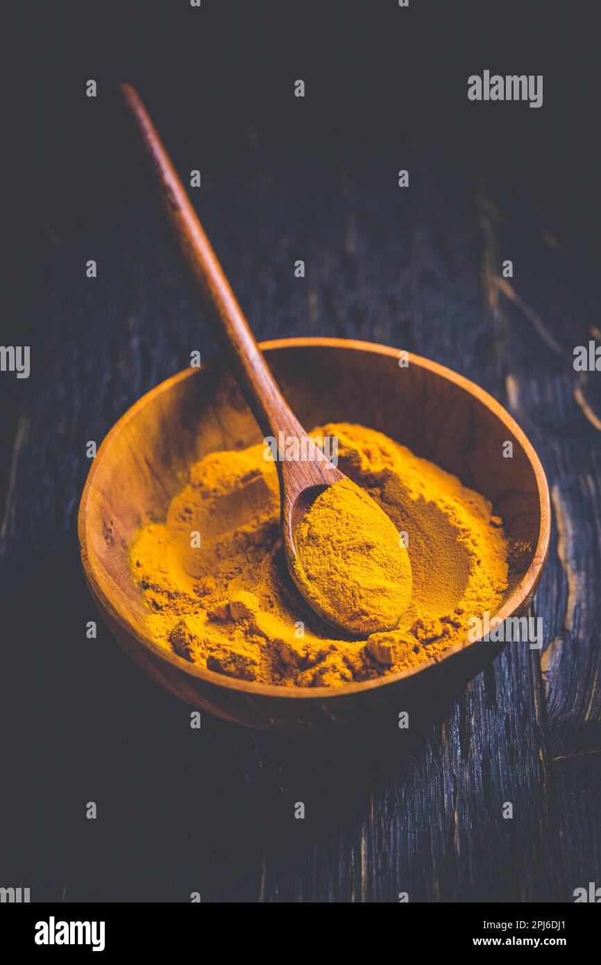 Indisches Kurkuma-Pulver, Kurkuma-Gewürz in kleiner Schüssel mit Löffel, Haldi-Pulver auf Holzhintergrund Stockfoto