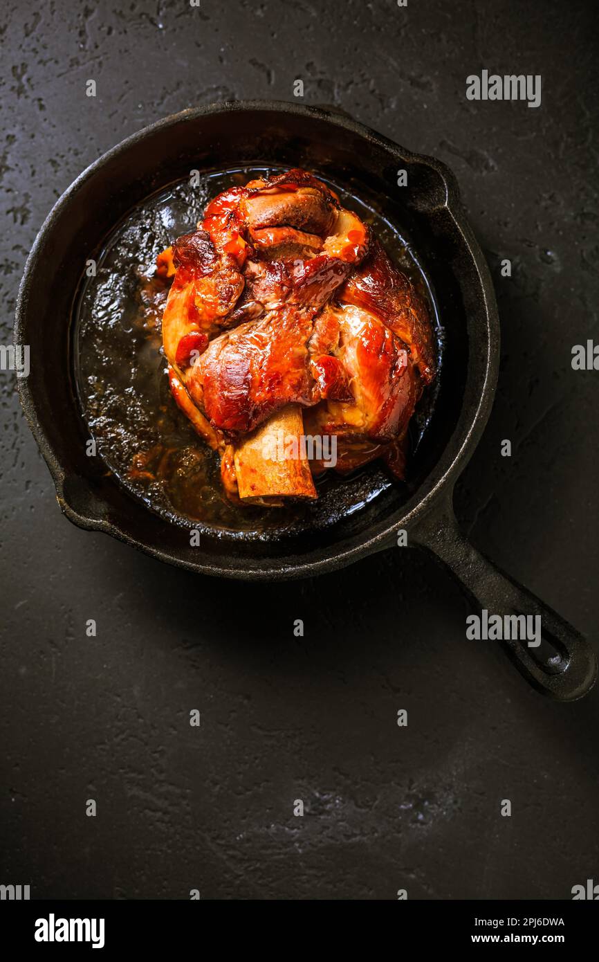 Traditionelle deutsche Küche - Gebratenes Schweineknöchel eisbein (Schweinshaxe) in einer Eisenkanne auf schwarzem Hintergrund Stockfoto