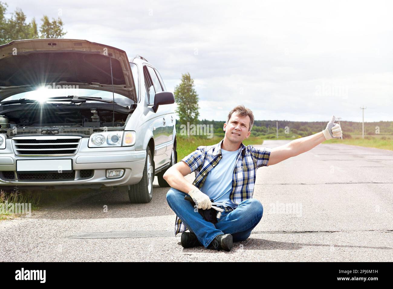 Mann mit Tools helfen und Daumen auftauchen, in der Nähe von seinem kaputten Auto Stockfoto