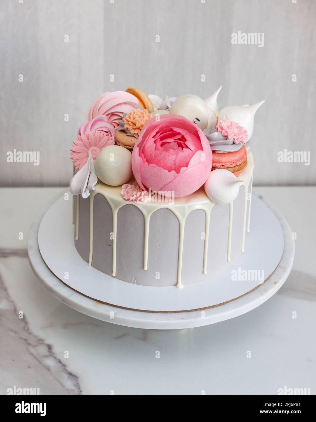 Wunderschöner und eleganter grauer Kuchen dekoriert mit geschmolzener weißer Schokolade, Makronen, pinkfarbenen Pfingstrosen, Kuchenpops und Süßigkeiten auf Marmorkakestand Stockfoto