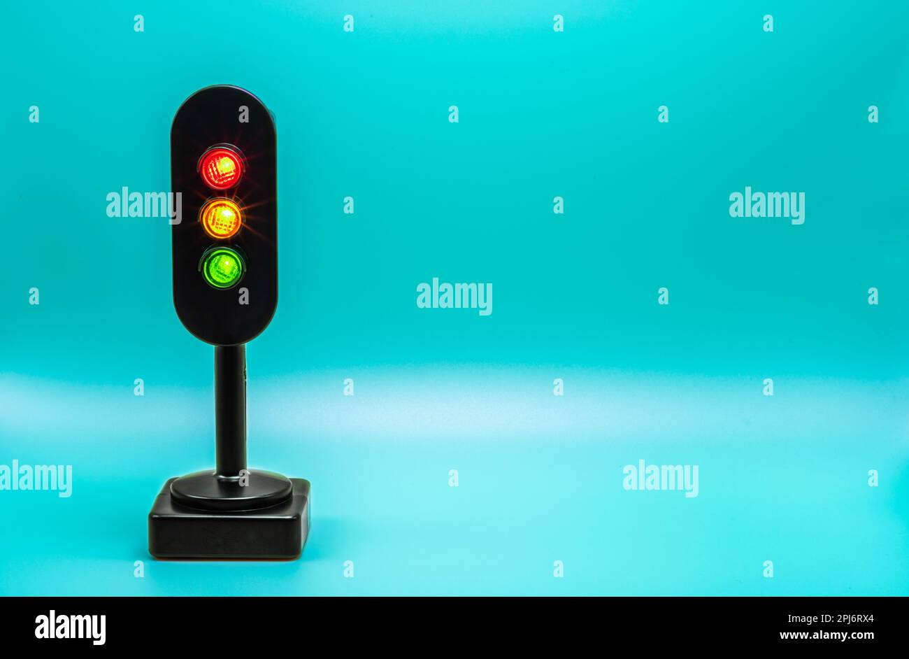 Miniatur-Ampel mit rotem, orangefarbenem und grünem Licht. Studioaufnahme. Himmlisch-hellblauer leerer Hintergrund. Stockfoto