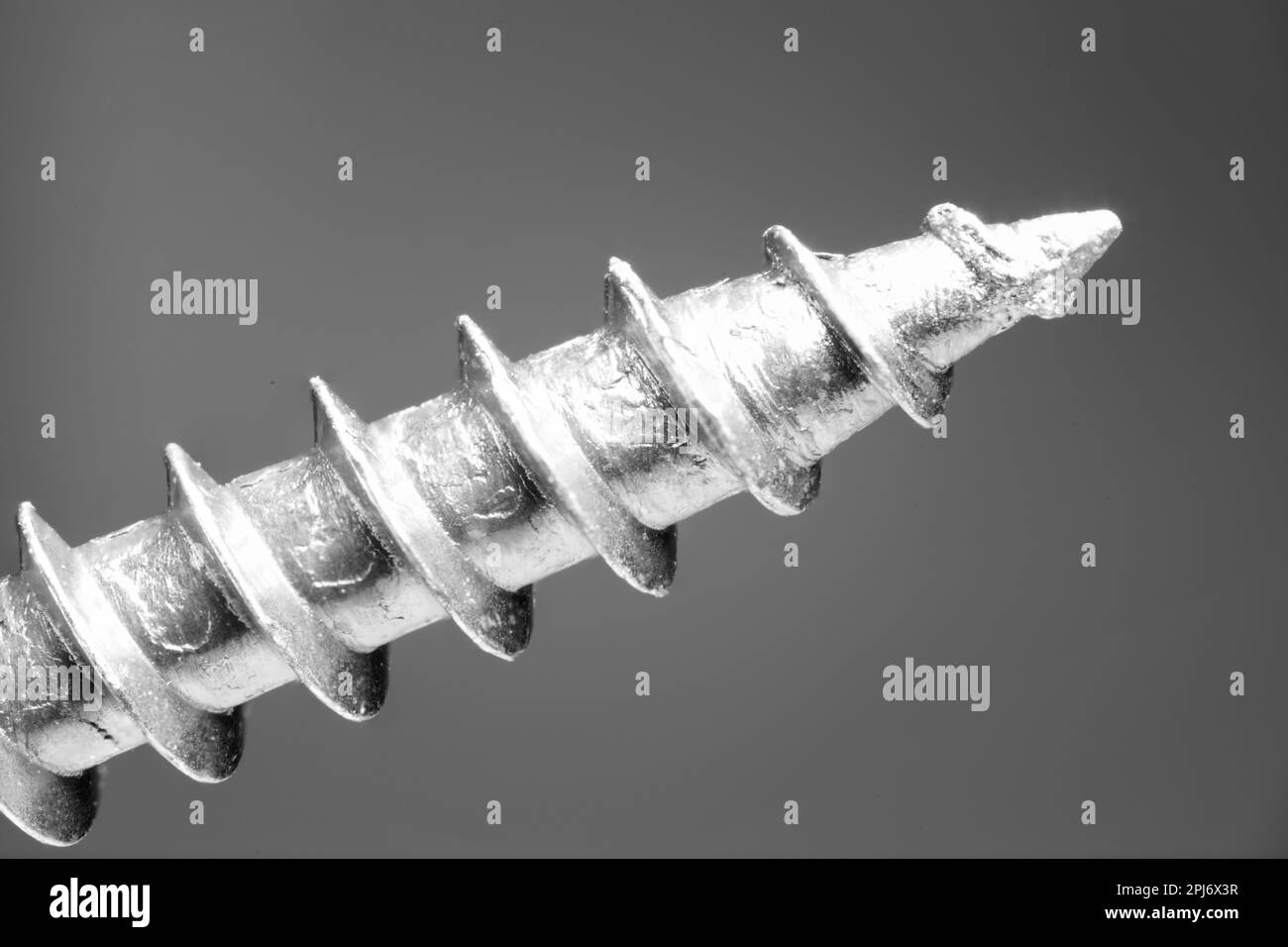 Spitze des gebogenen Gewindes einer Metallschraube als extrem-Makro-Nahaufnahme diagonal im Bild als Konzept für Gewindeschraubenhandwerk und Bohren Stockfoto