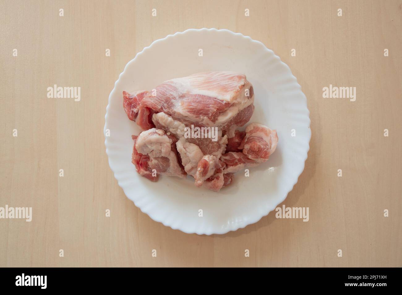 Ein Stück rohes Schweinefleisch liegt auf einem weißen Teller auf dem Tisch Stockfoto