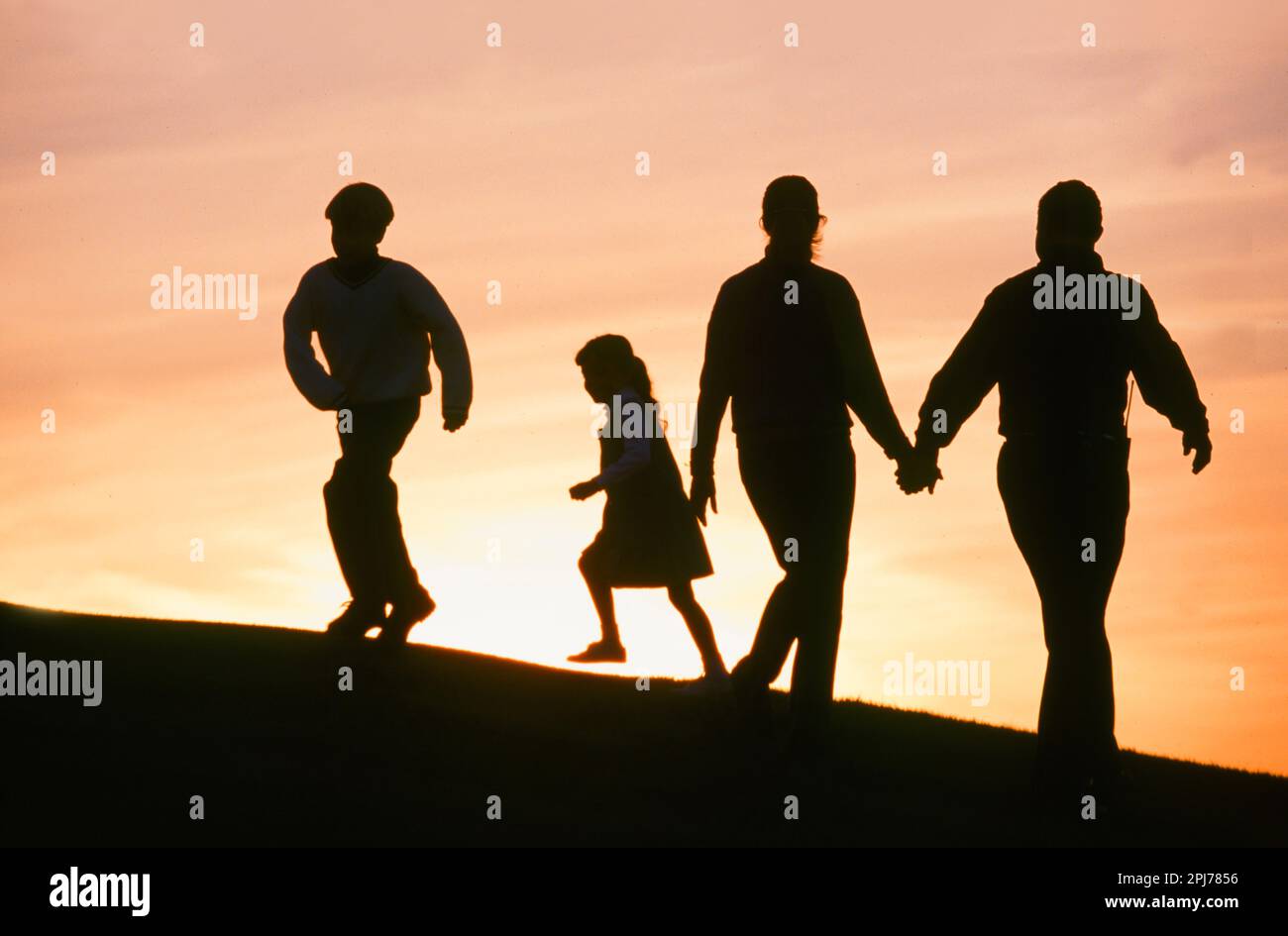 Silhouette einer vierköpfigen Familie, die bei Sonnenuntergang auf einem Hügel spaziert Stockfoto