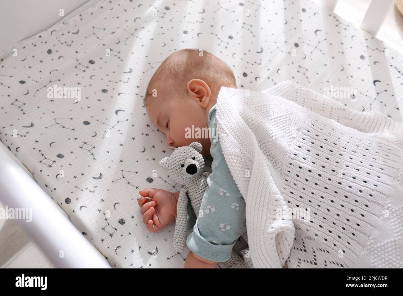 Niedliches Baby mit Spielzeug, das friedlich im Kinderbett schläft, über der Aussicht Stockfoto