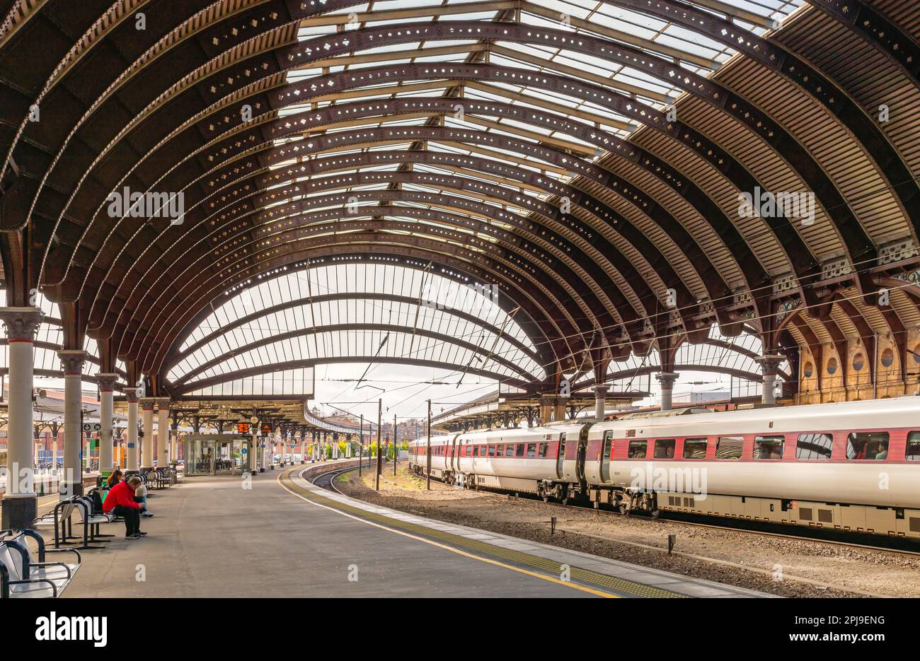 Panoramablick auf einen Bahnhof mit einem historischen prunkvollen Eisendach aus dem 19. Jahrhundert. Ein Zug befindet sich neben einem Bahnsteig, und die Schienen krümmen sich in die Ferne. Stockfoto