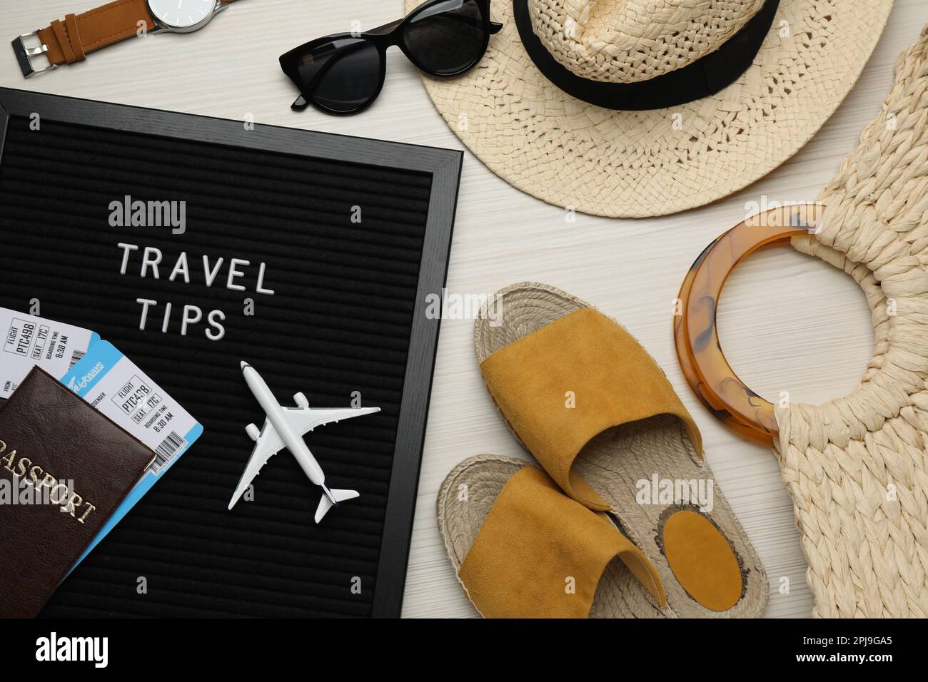 Schwarzes Brieftafel mit Reisetipps und Touristengegenständen auf weißem Holztisch, flach liegend Stockfoto