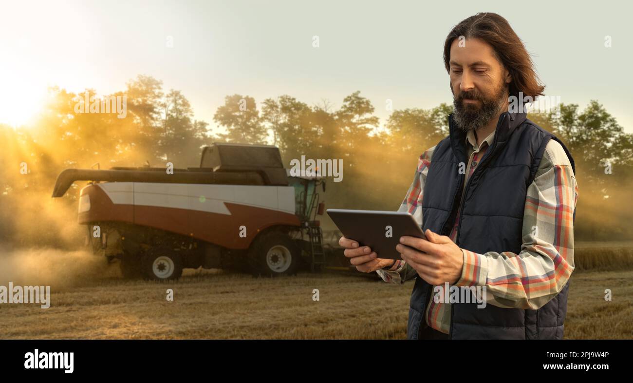 Landwirt mit digitalem Tablet im Hintergrund der Erntemaschine. Konzept der intelligenten Landwirtschaft. Hochwertiges Foto Stockfoto