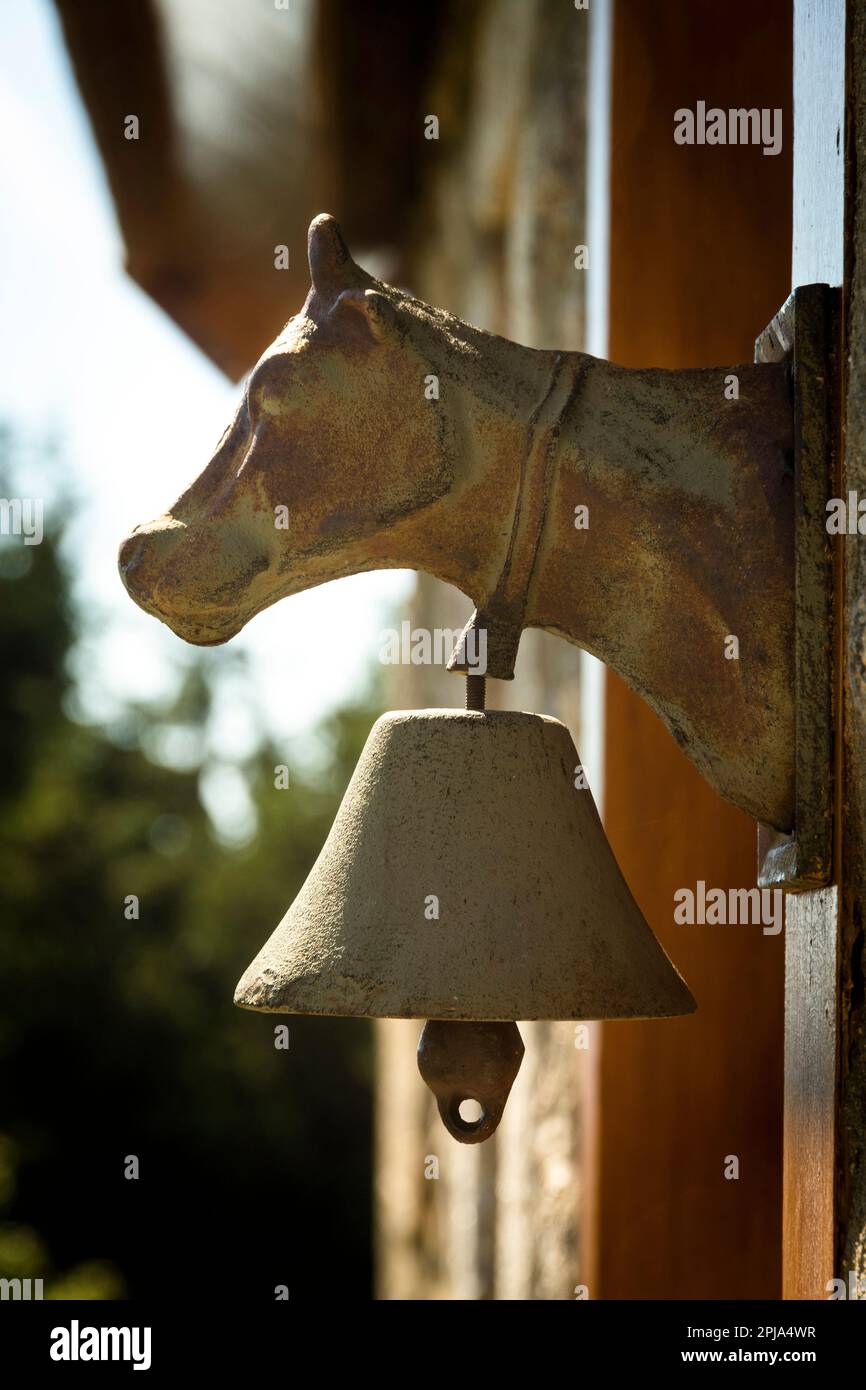 Rustikale kuhförmige Glocke an einer Holzwand in einem Landhaus bei Tageslicht, Auvergne, Frankreich Stockfoto